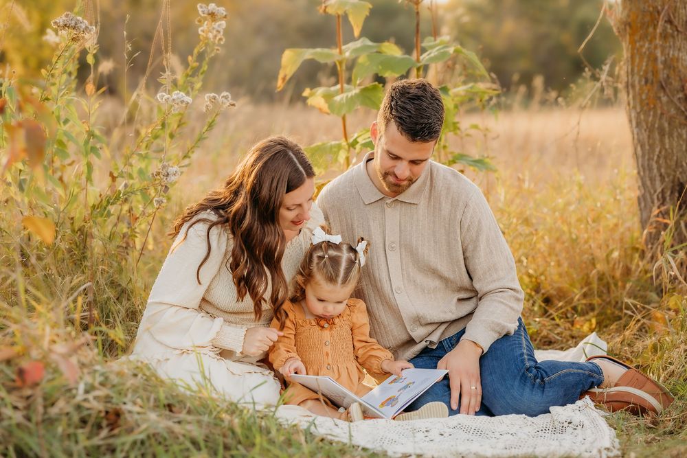 A couple lies on a blanket in a golden field during sunset, sharing intimate moments together during their outdoor photoshoot.
