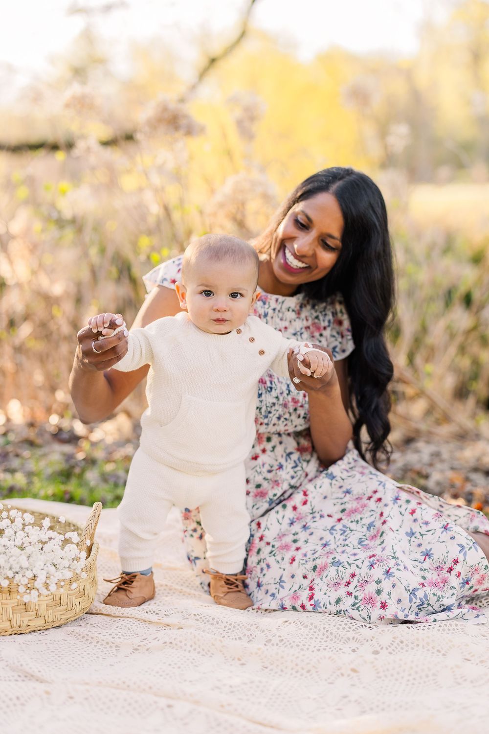 Mother and baby sit on blanket outdoors during autumn photoshoot with natural golden lighting.