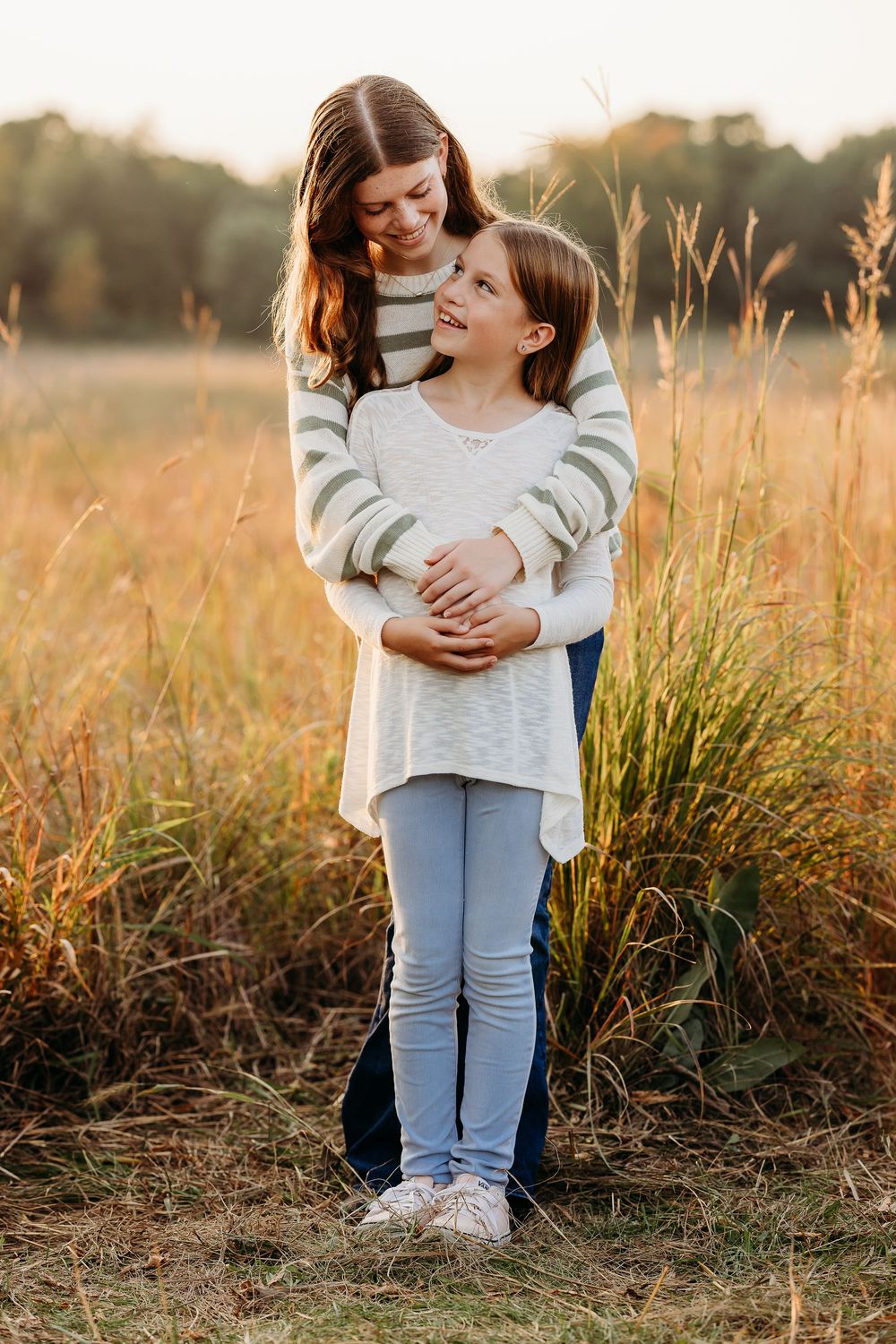 Two people share a tender embrace while standing in a golden field at sunset.
