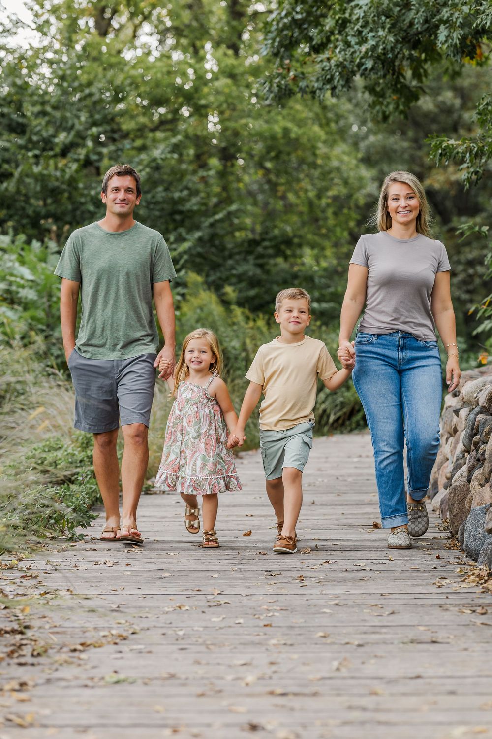 A family walks together on a stone path through a park on a sunny summer day.