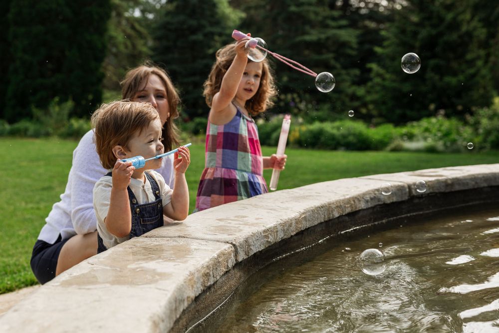 Children blowing bubbles at edge of fountain in summer garden.