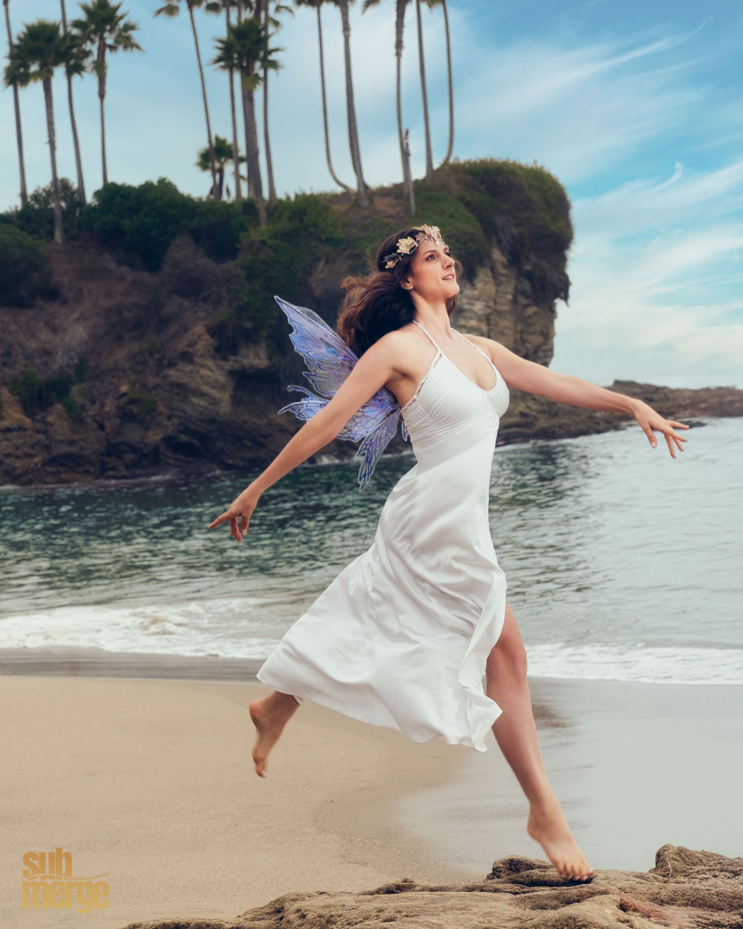 A figure in a flowing white dress dances gracefully on a tropical beach with tall palm trees and cliffs in the background.