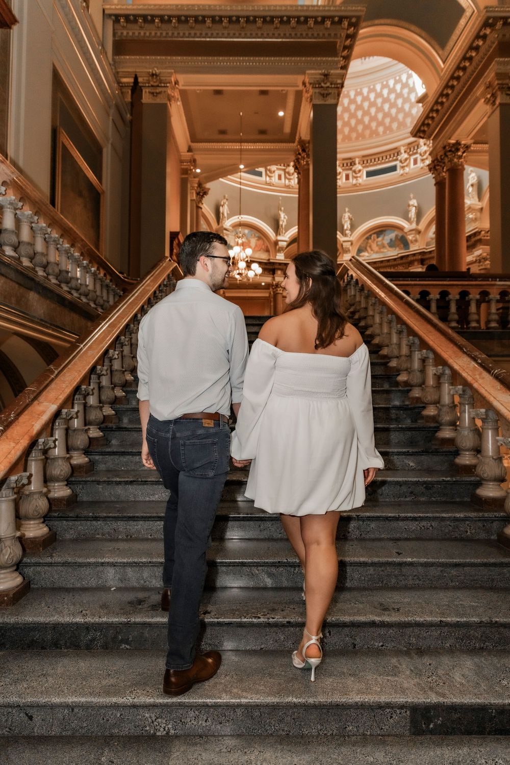 Engaged couple walking up the stairs at the Iowa State Capital