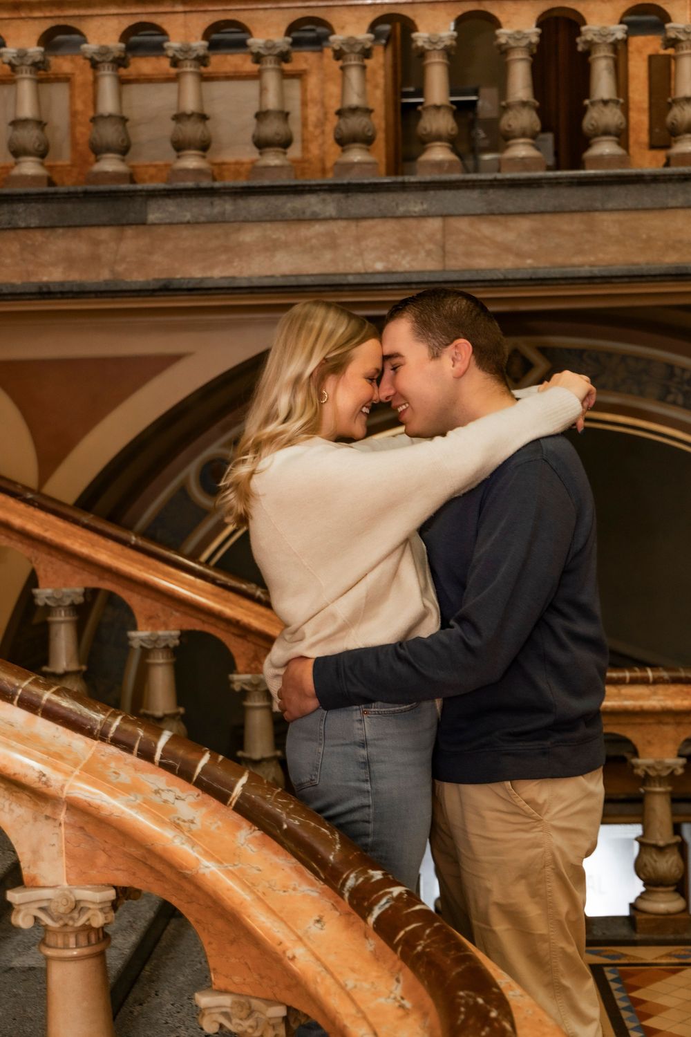 Couple embracing on the large staircase at the Iowa State Capital Building during their engagement session.