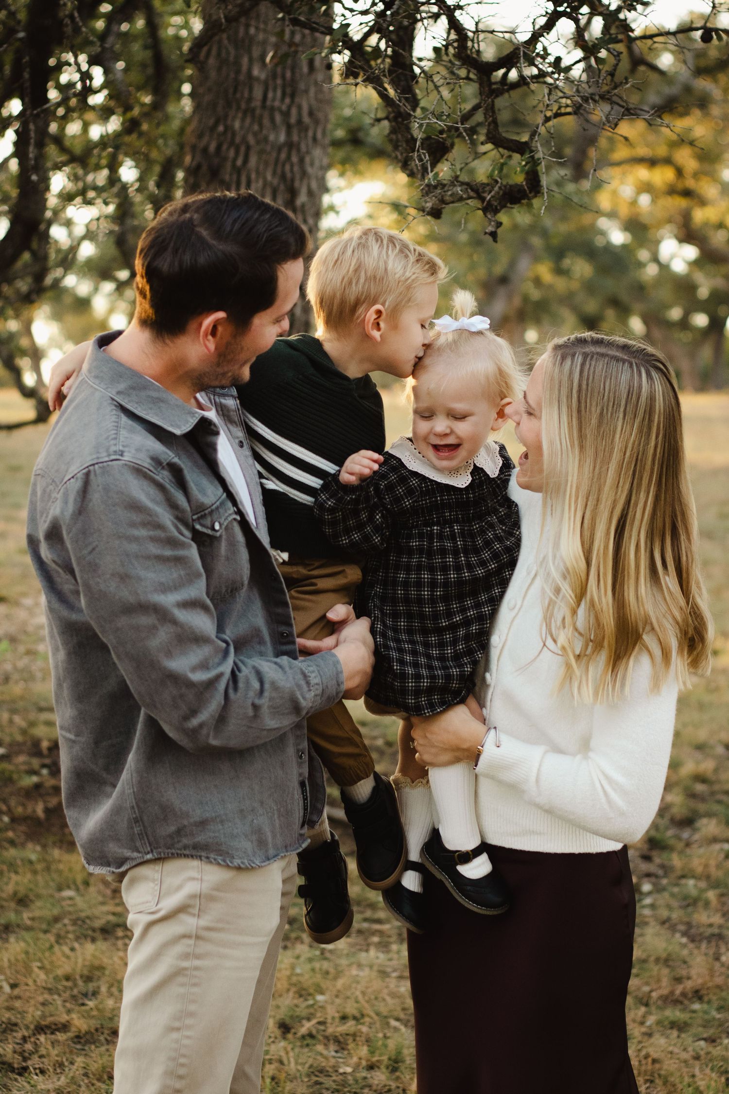 A family shares a joyful moment together outdoors in autumn light among trees.