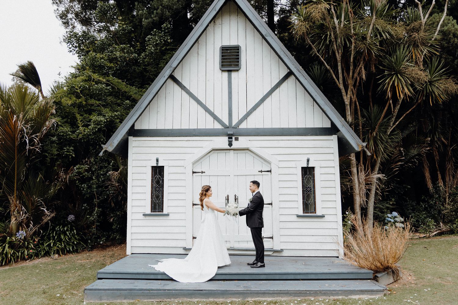 A white chapel wedding ceremony takes place on a small stage captured by Apertured Media Auckland Wedding Photographer.