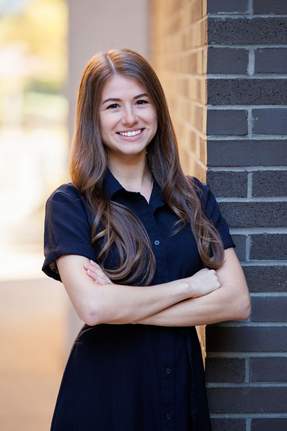 Professional headshot of woman in black shirt smiling against brick wall background.