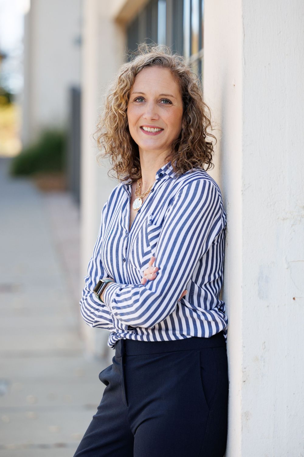 Professional woman in striped button-down shirt poses against white building exterior.