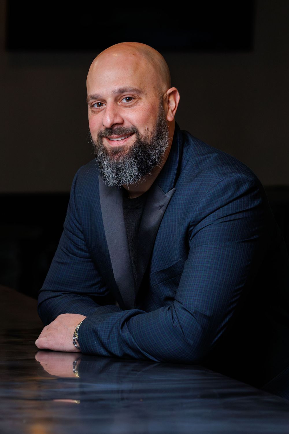 Professional portrait of a business person in a navy suit with a salt-and-pepper beard smiling at camera.