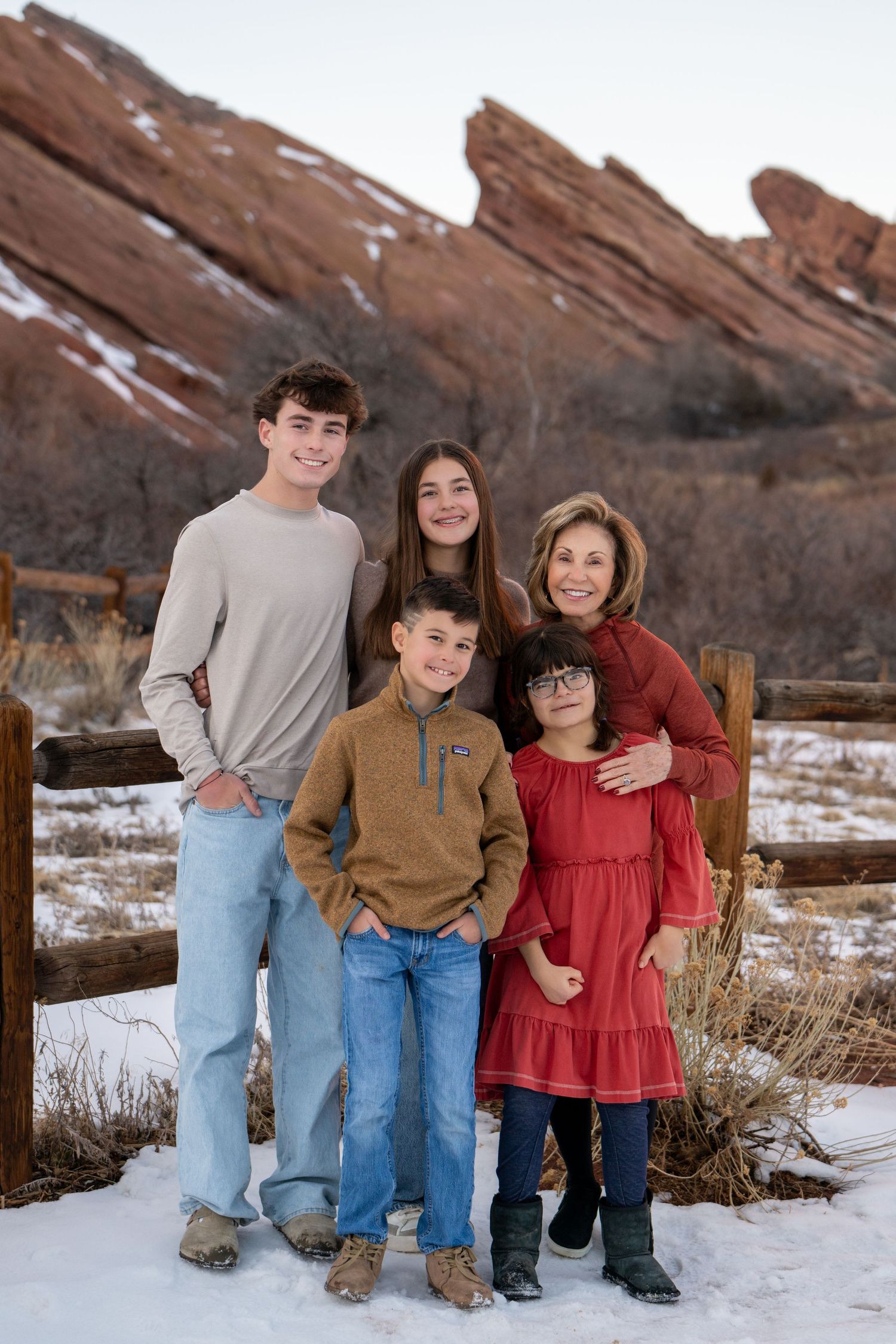 A group poses together in winter against striking red rock formations at Red Rocks Park with snow on the ground.