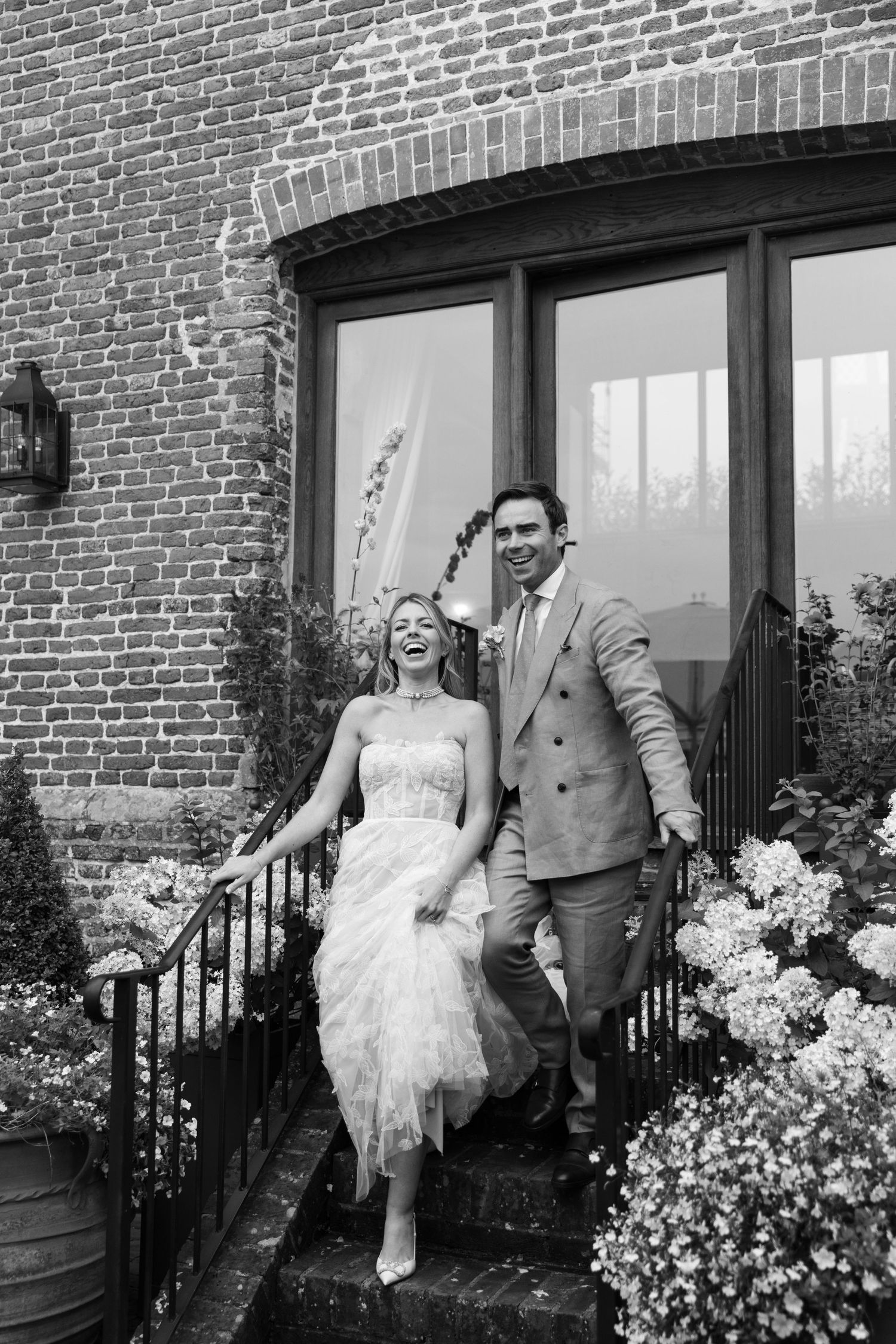 A couple standing on brick steps in vintage-inspired wedding attire outside a historic building.