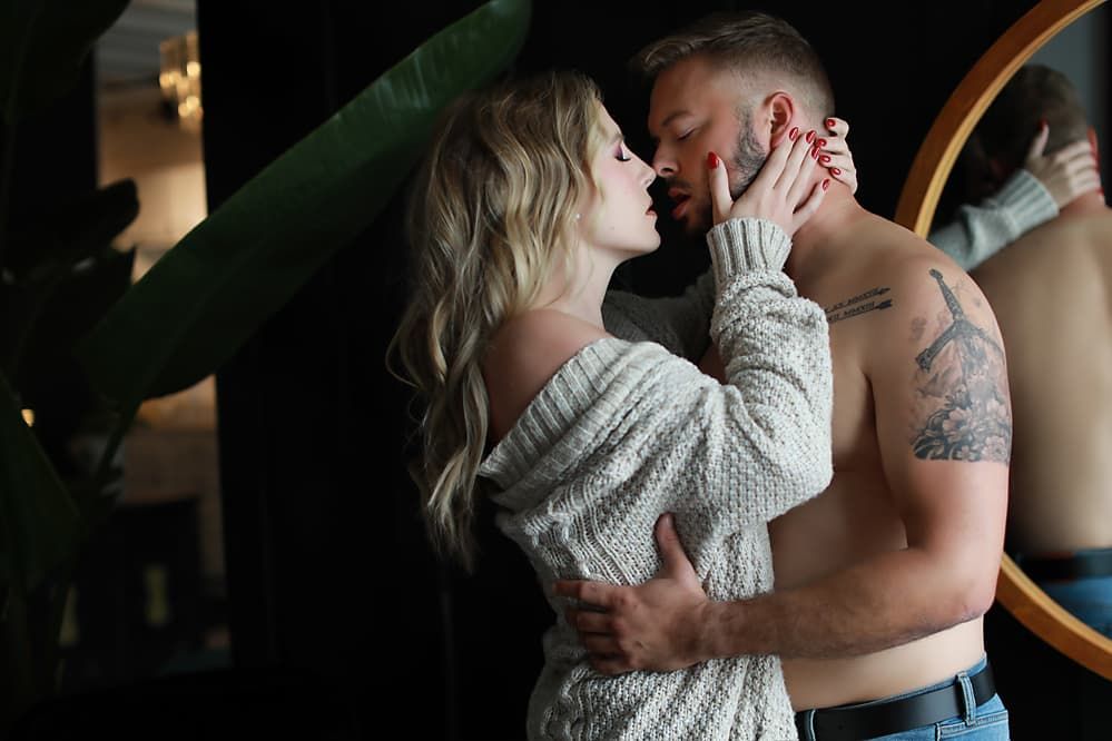 Intimate portrait of couple embracing, with woman in knit sweater against dark background.