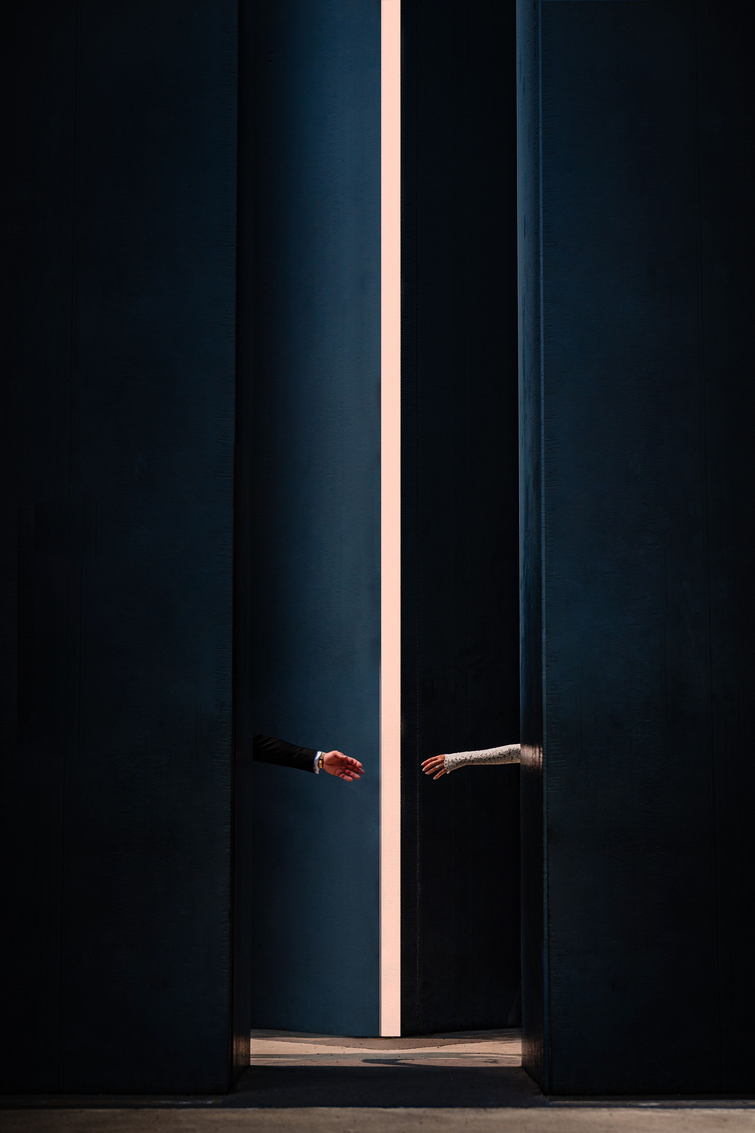 Dramatic lighting through a narrow doorway gap revealing hands reaching towards each other.