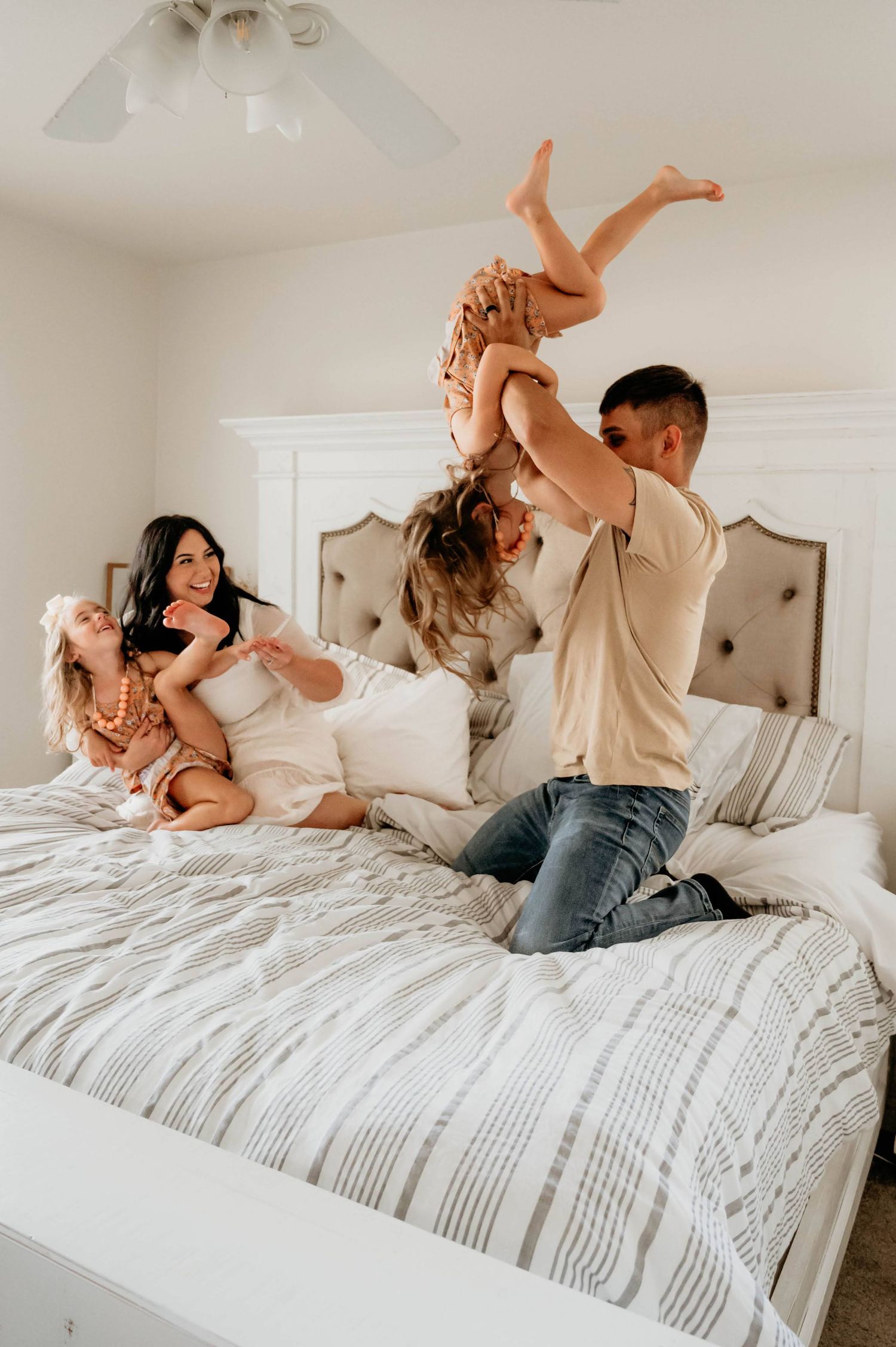 Playful family moment with children being lifted on white bed with decorative headboard rockford il