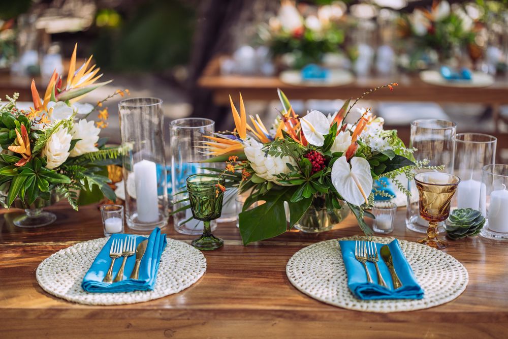 Tropical wedding table setting with bright Birds of Paradise flowers, white placemats, and turquoise napkins on wooden table.
