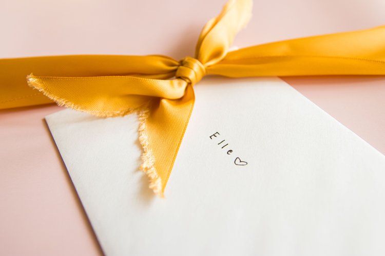 Elegant white envelope with gold ribbon on pink background.