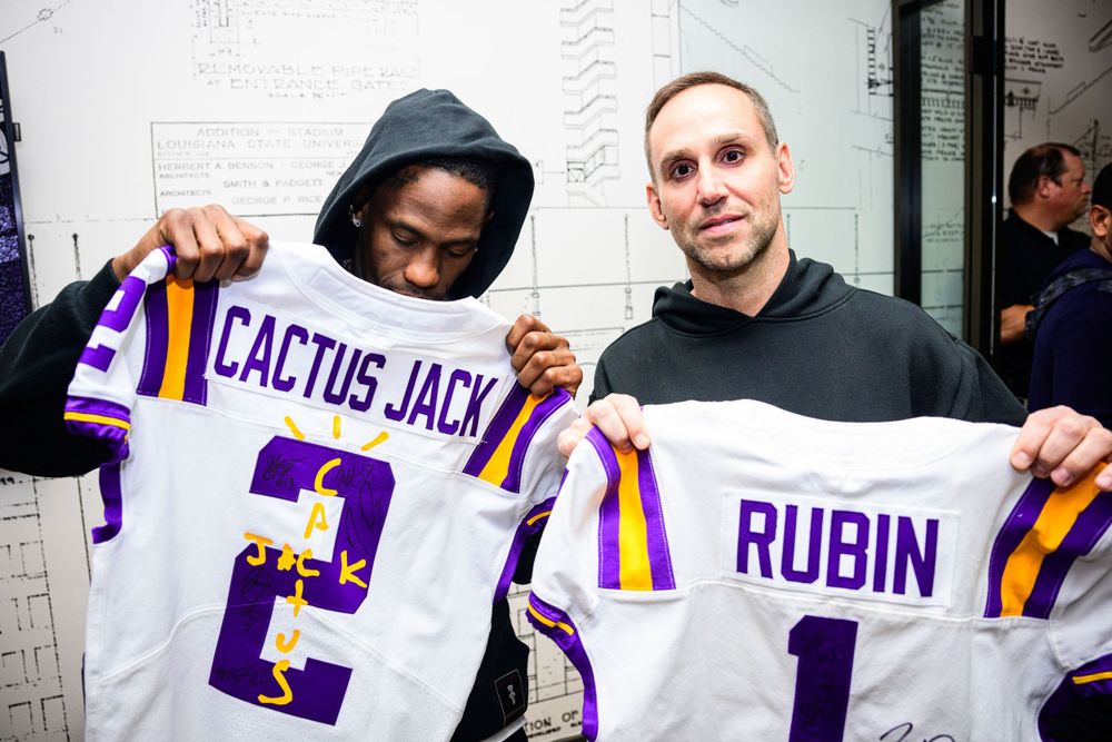 Two people hold up LSU sports jerseys with Cactus Jack and Rubin names.