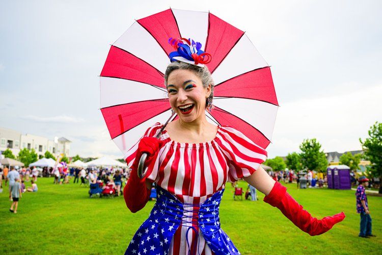Performer in patriotic costume with red and white striped fan celebrates at outdoor festival.