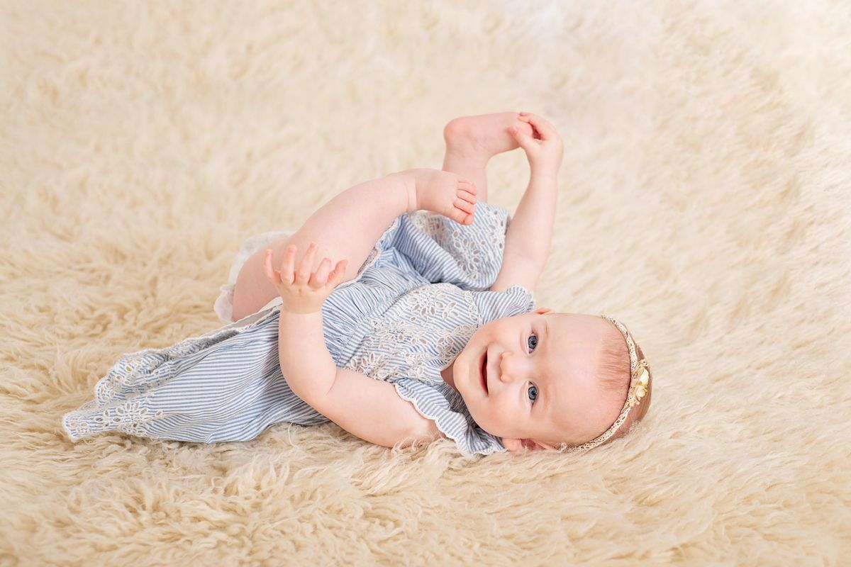6 month baby girl lays on back smiling at camera for milestone photoshoot