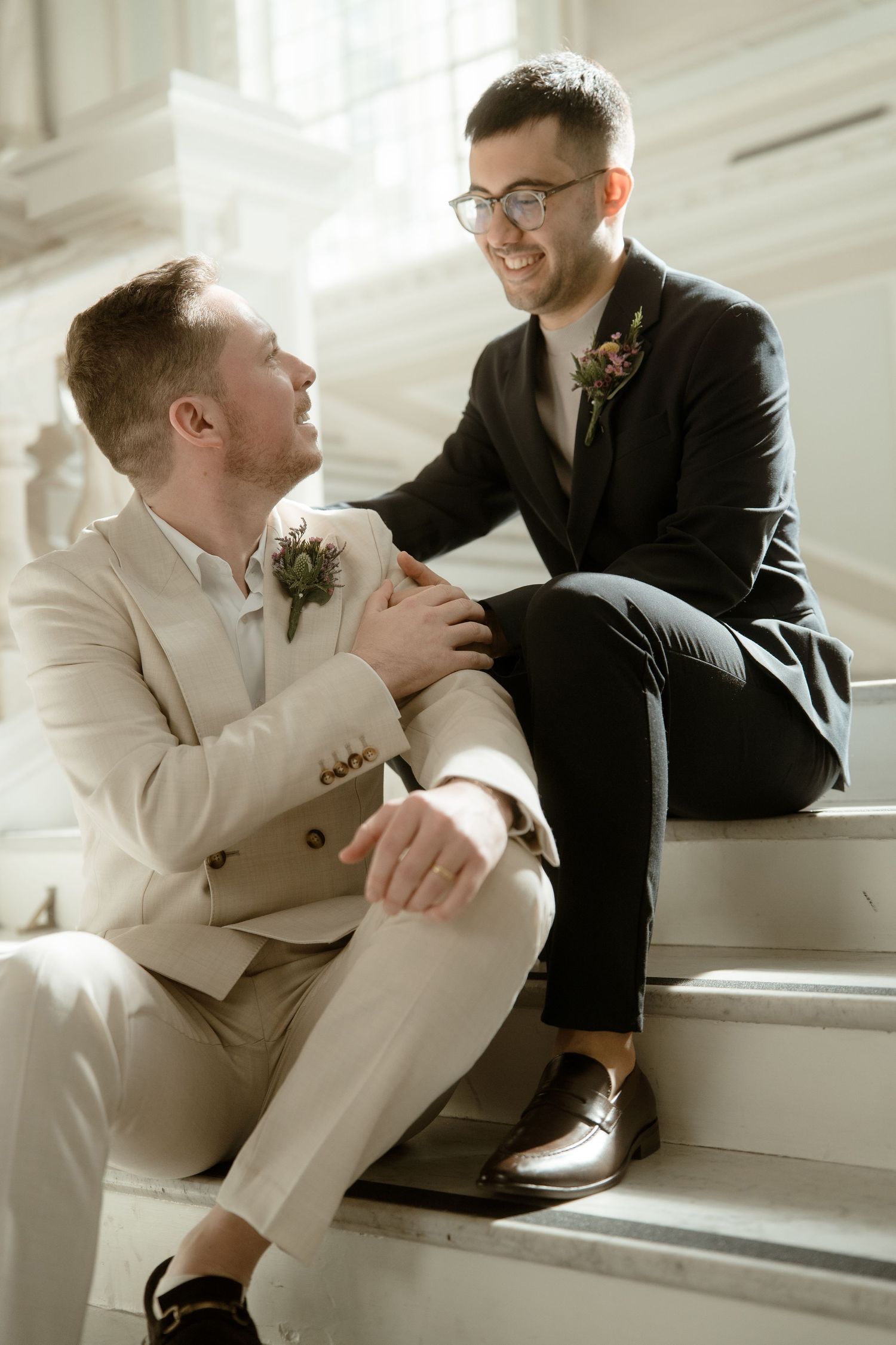 Wedding couple sharing candid moments while sitting on white stairs.