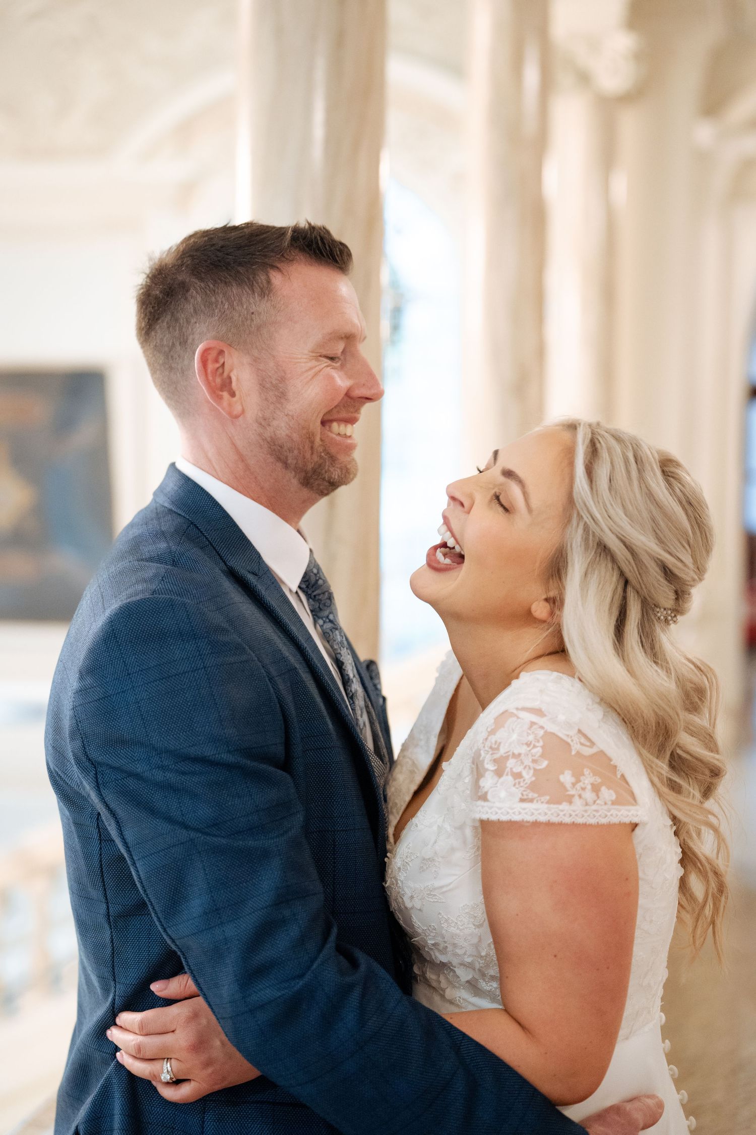 Joyful wedding couple sharing a laugh in a bright, elegant indoor setting.