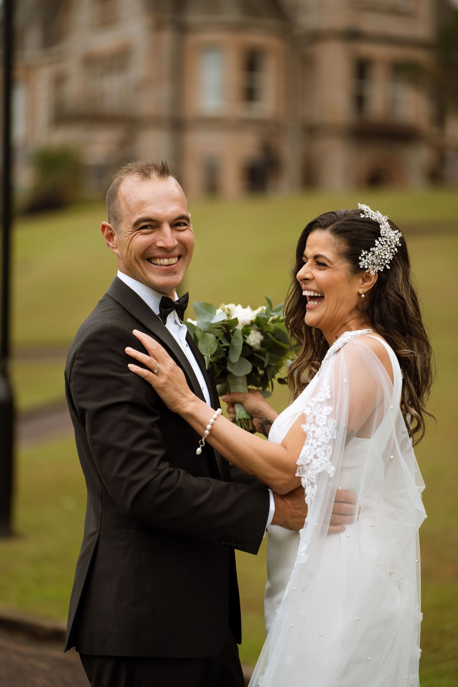 A couple shares an intimate moment during their wedding photoshoot on the grounds of a historic building.