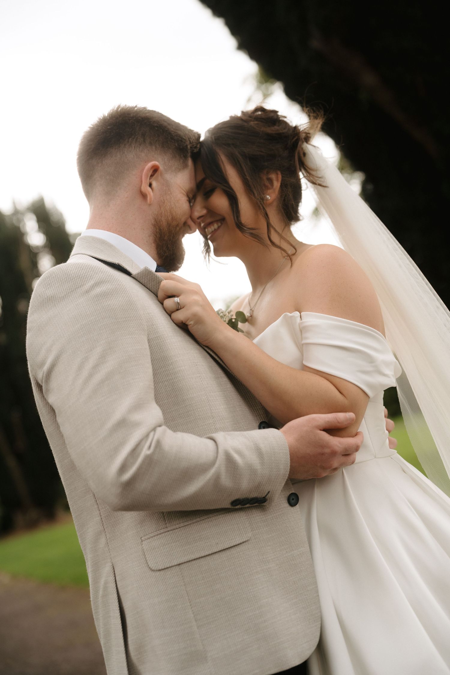 Romantic wedding couple embraces and kisses during outdoor photo session in a park setting.