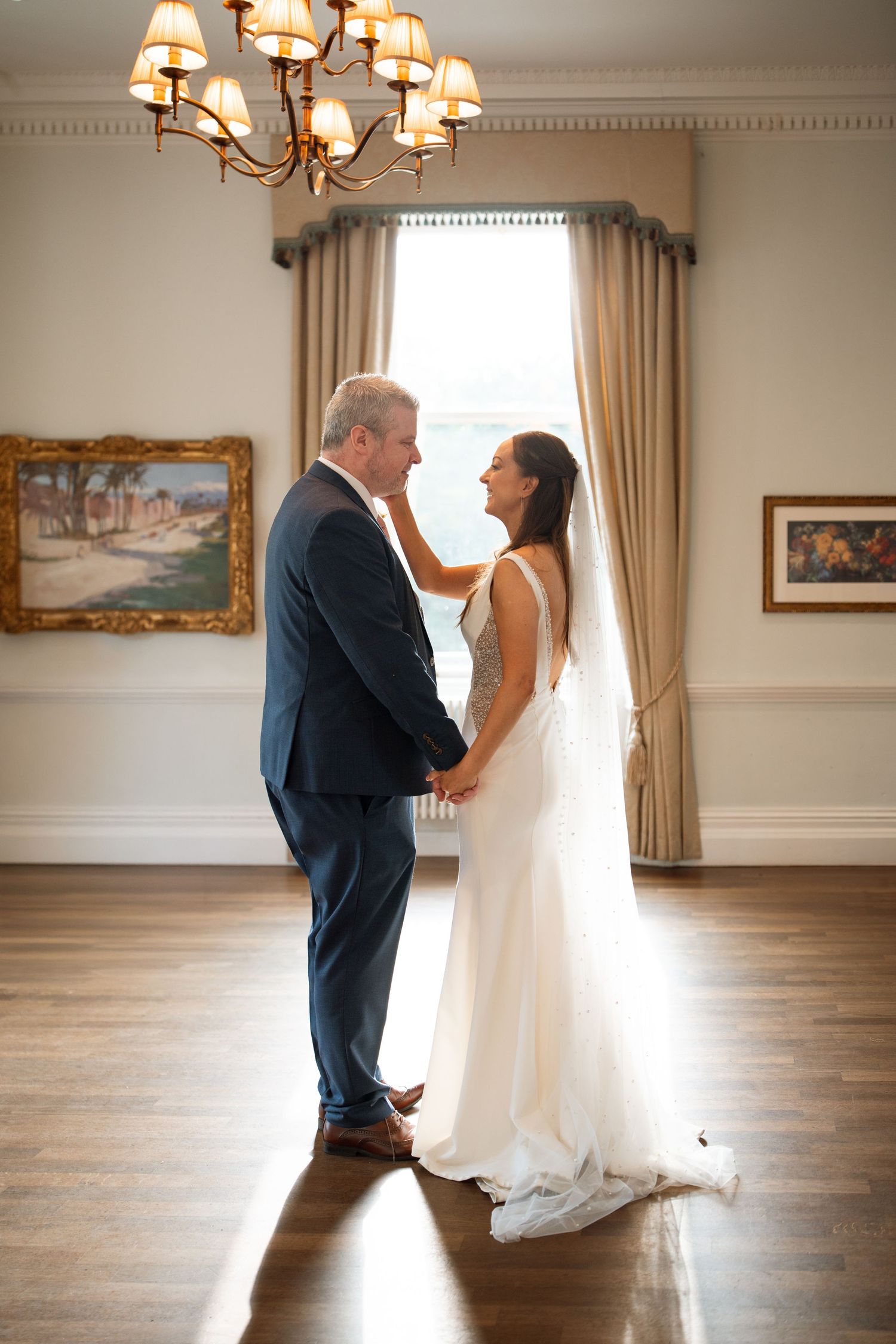 Tender moment between newlyweds in an elegant room with warm lighting and artwork.