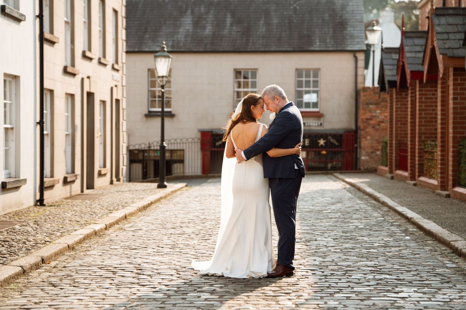 Romantic wedding portrait on a cobblestone street with historic buildings.