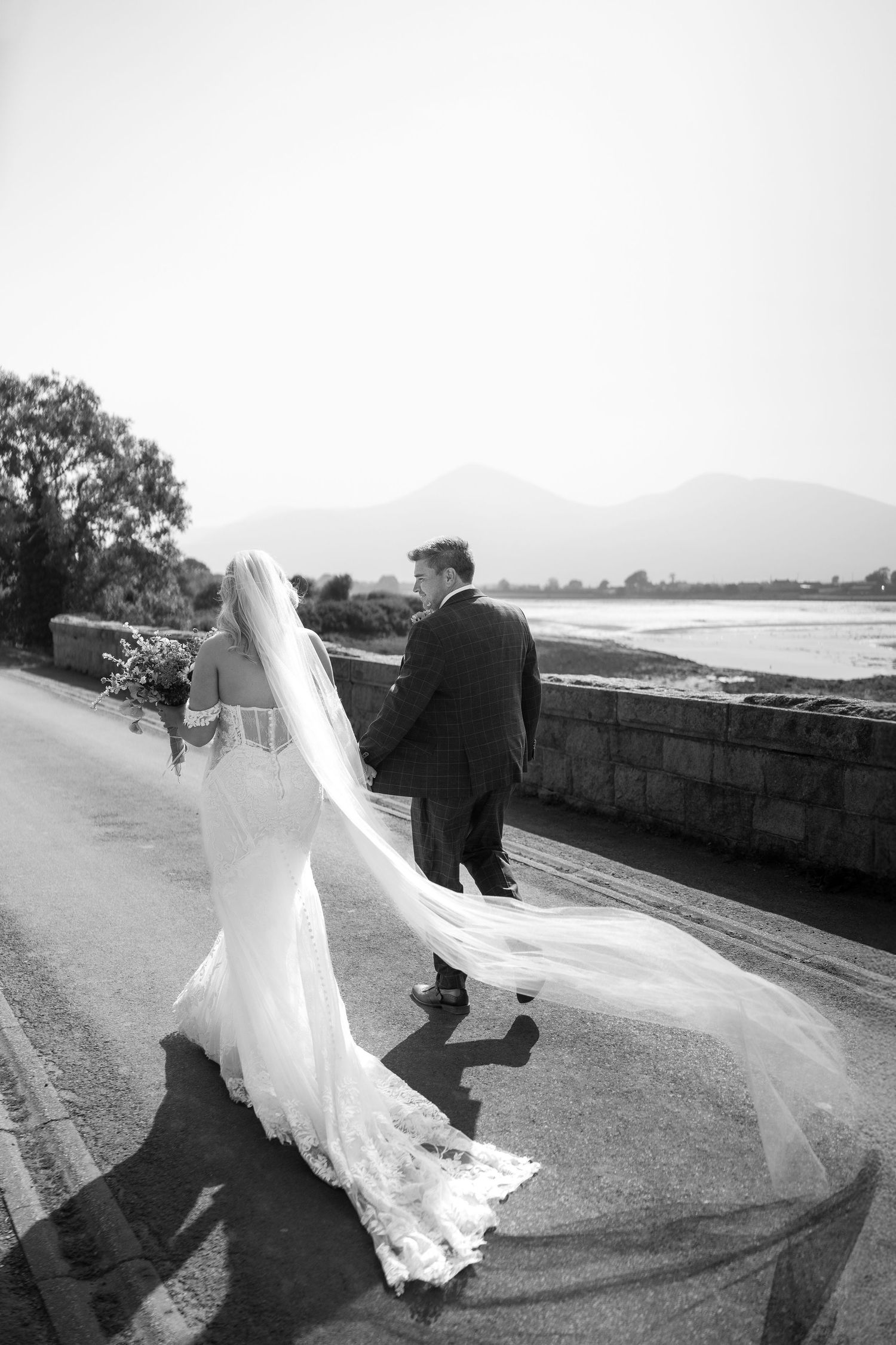 Dramatic black and white photo of a bride's flowing veil along a coastal path.