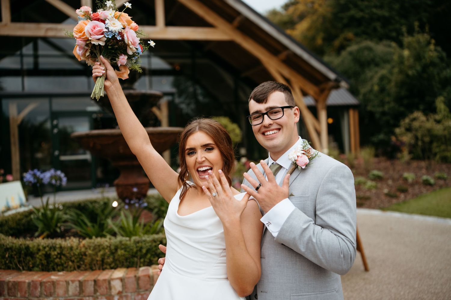 A couple celebrates their wedding day with joyful expressions outside a rustic wooden venue.