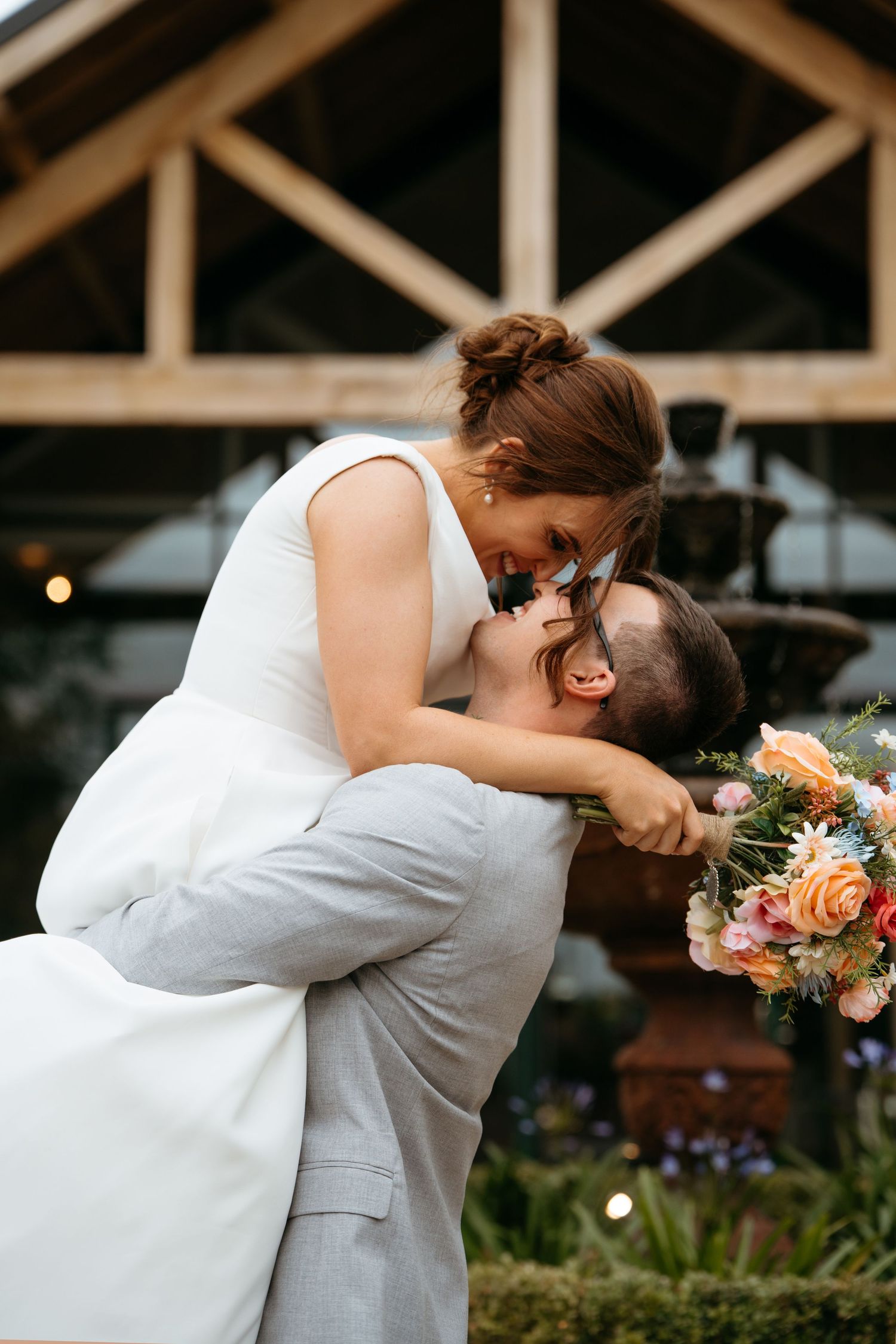 A romantic dip kiss between newlyweds with the bride holding a colorful bouquet.