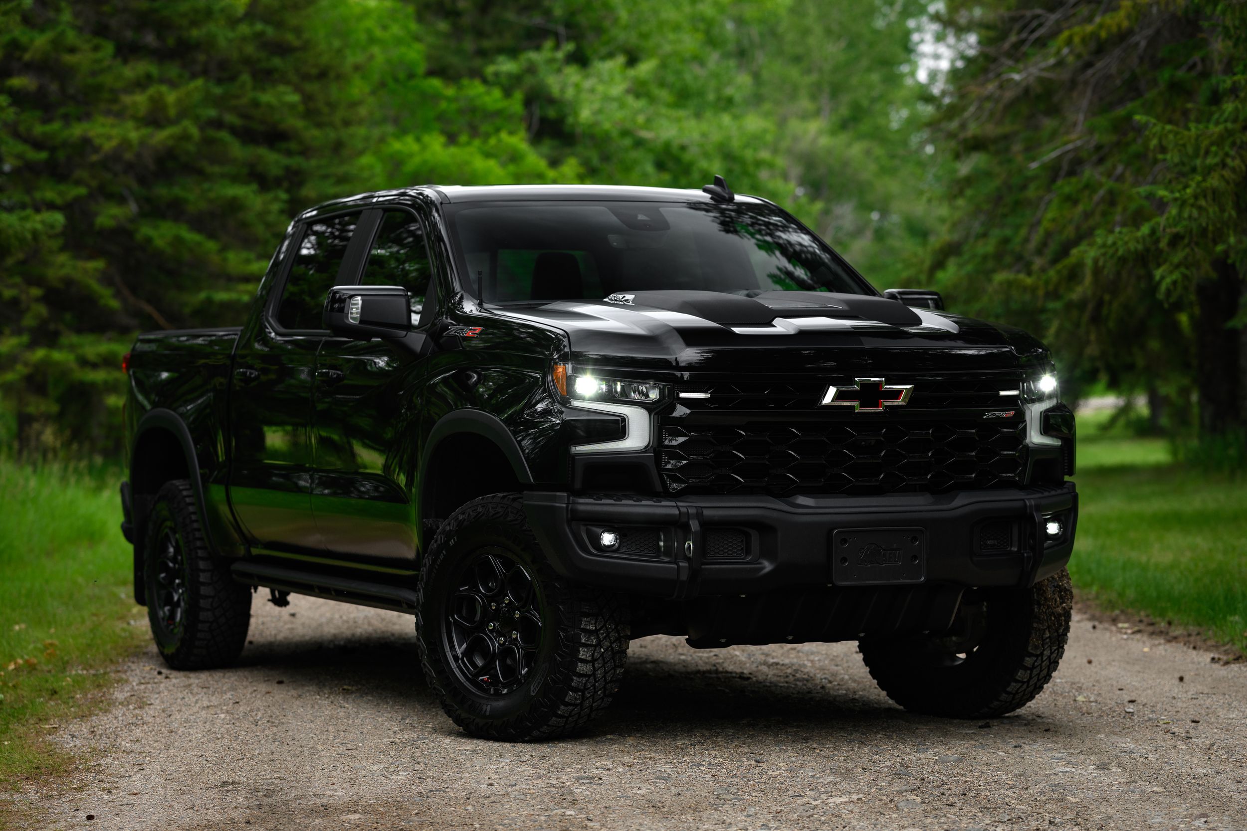 A sleek black Chevrolet Silverado pickup truck with custom wheels parked on a forest path in natural surroundings.