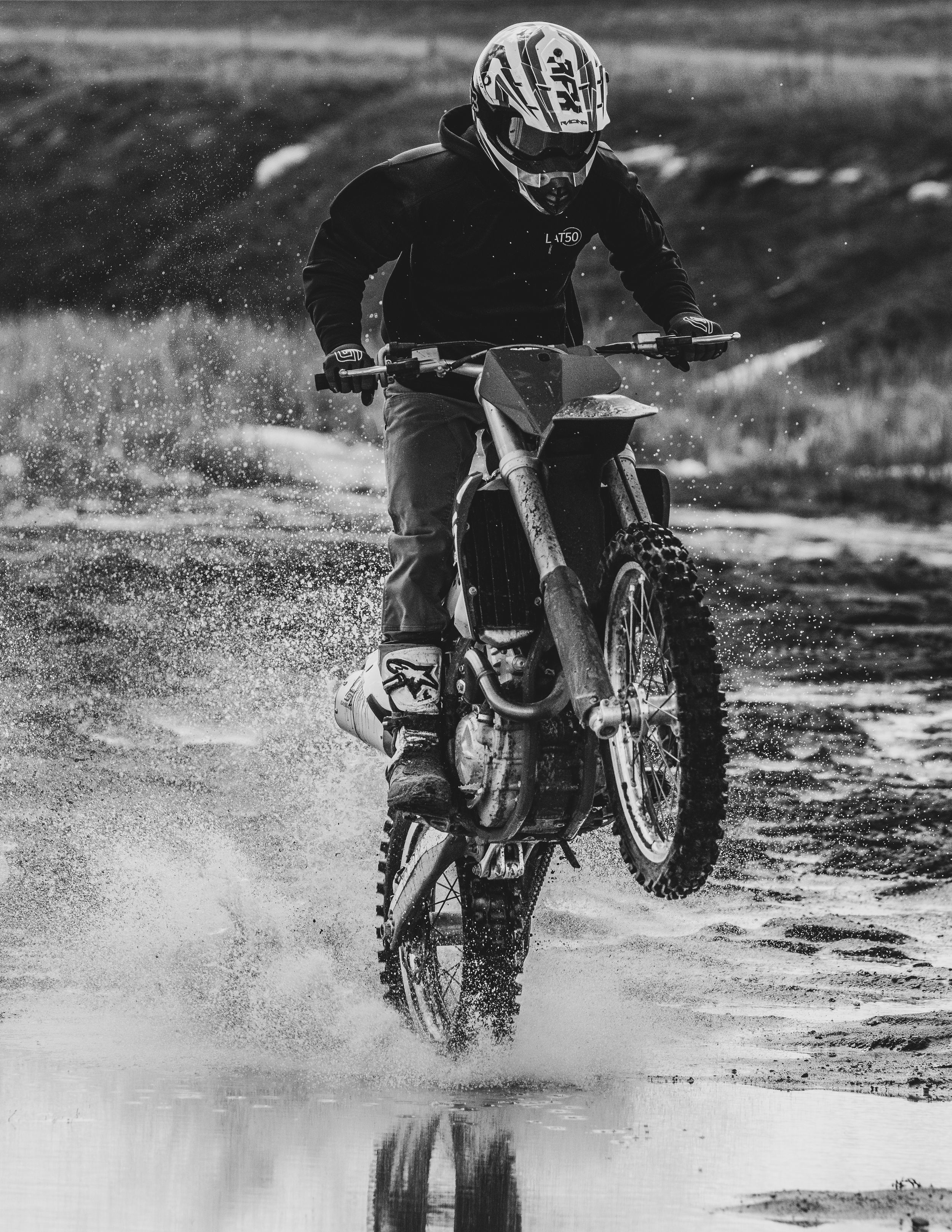 A dirt bike rider performs a dramatic splash through muddy water in black and white monochromatic photography.