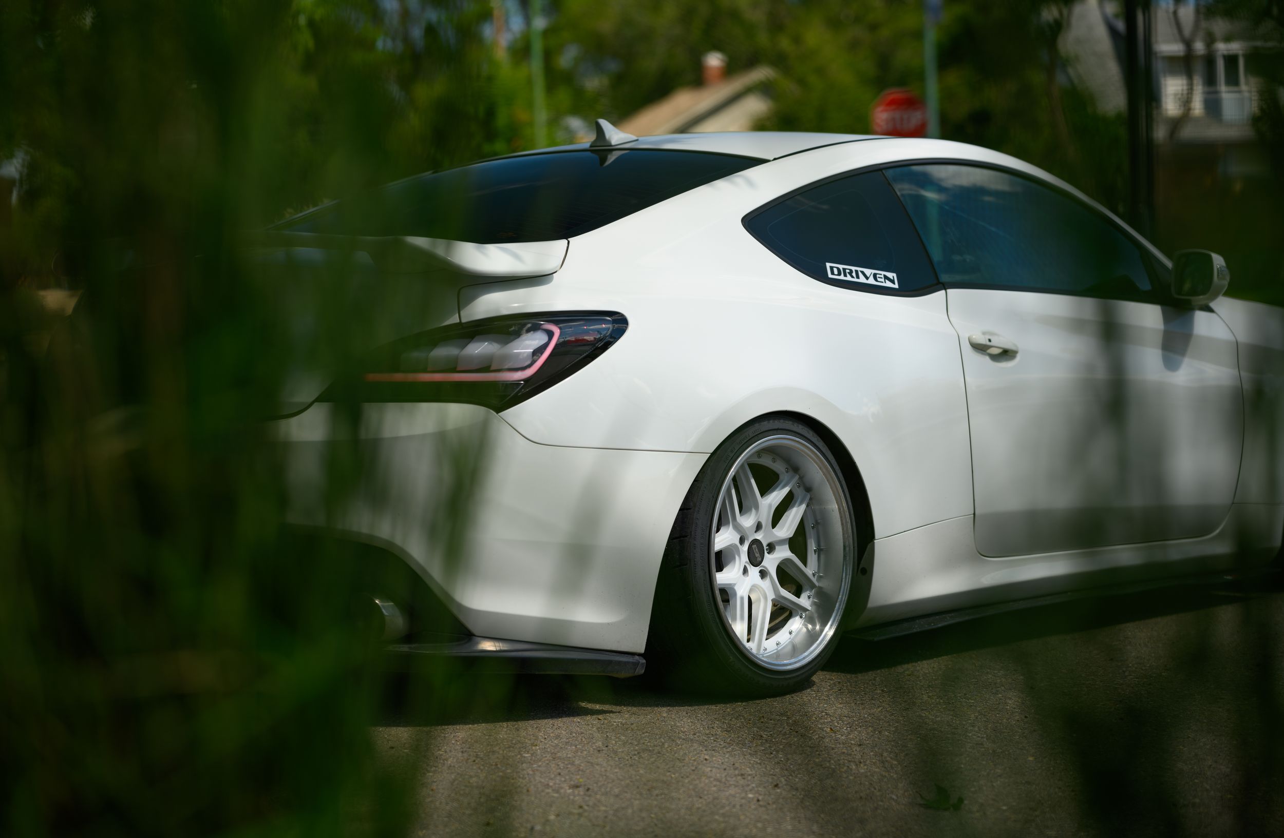 White sports sedan with custom wheels and lowered suspension viewed from the rear quarter.