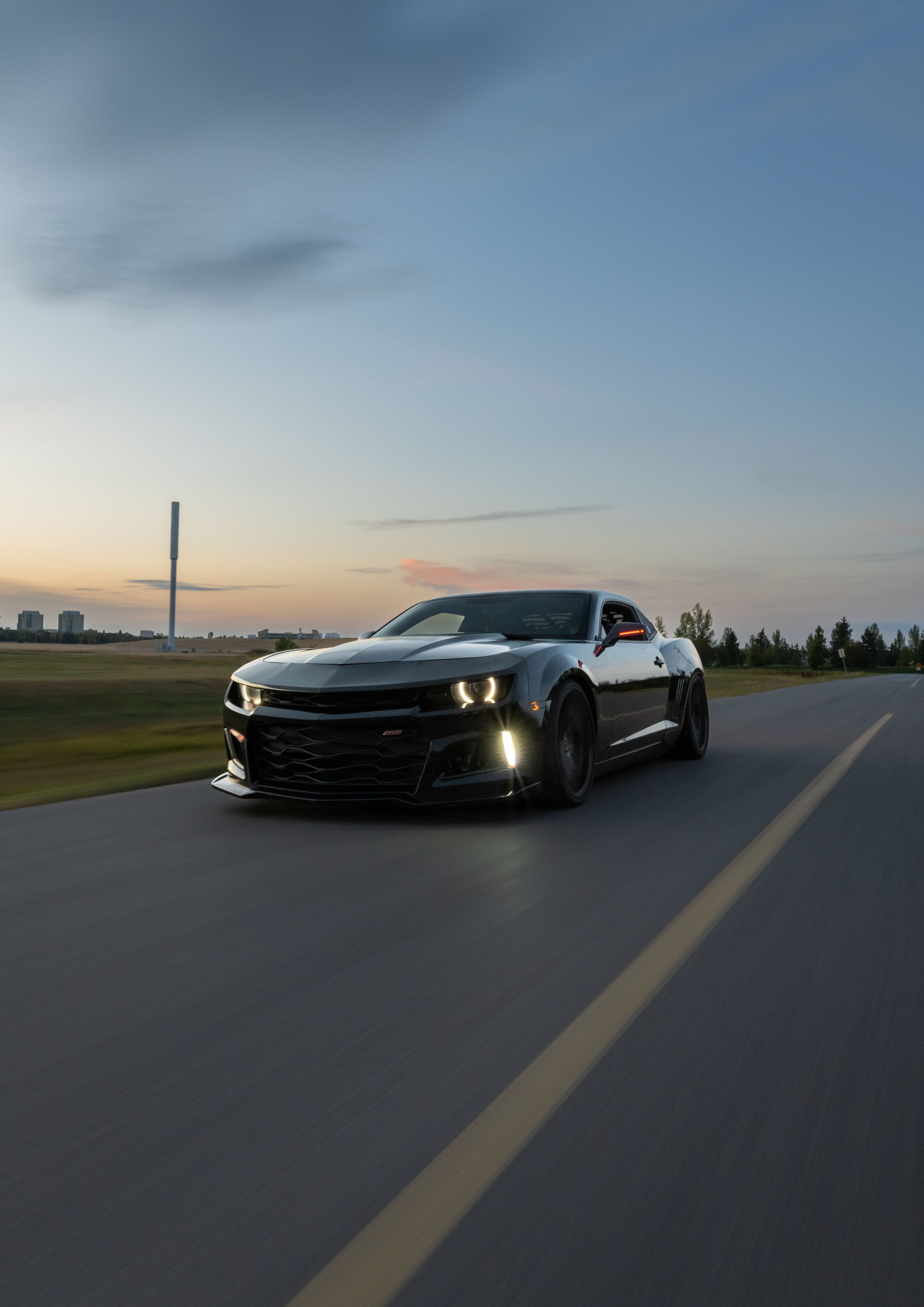 Black Chevrolet Camaro with headlights on photographed at dusk.