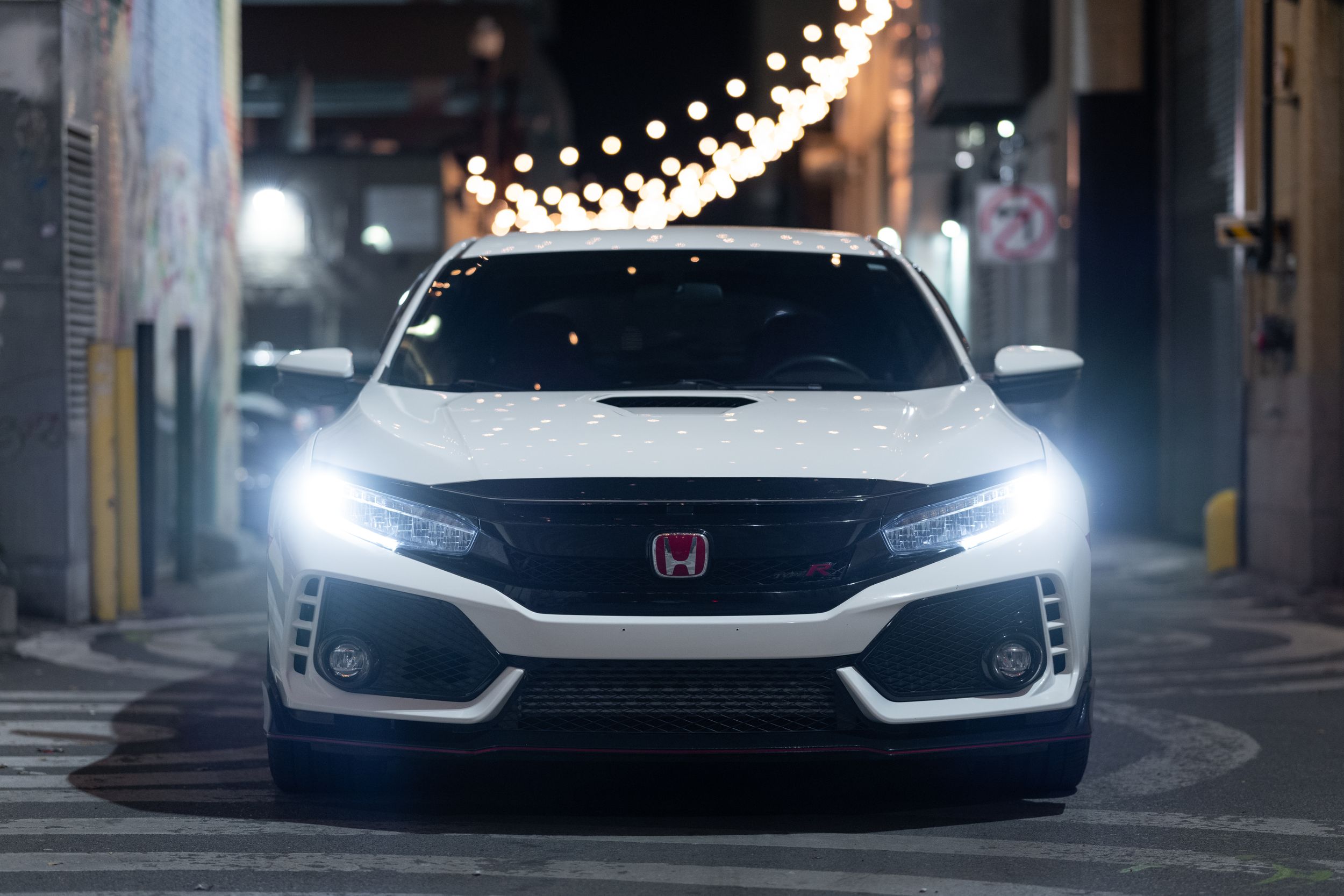 White Honda Civic Type R with bright LED headlights parked at night under string lights.