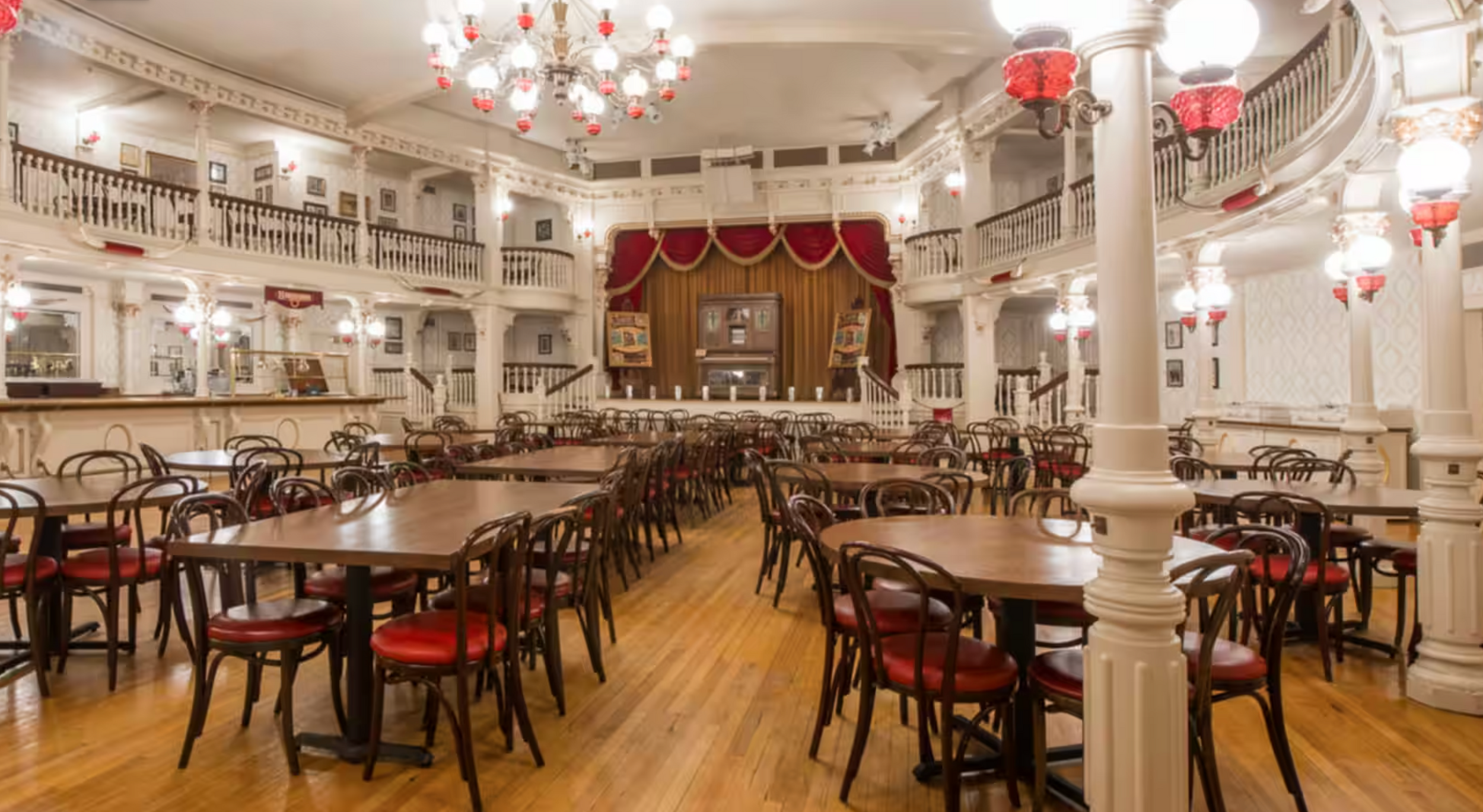 Panoramic view of an elegant banquet hall with wooden tables, white columns, and crystal chandeliers.