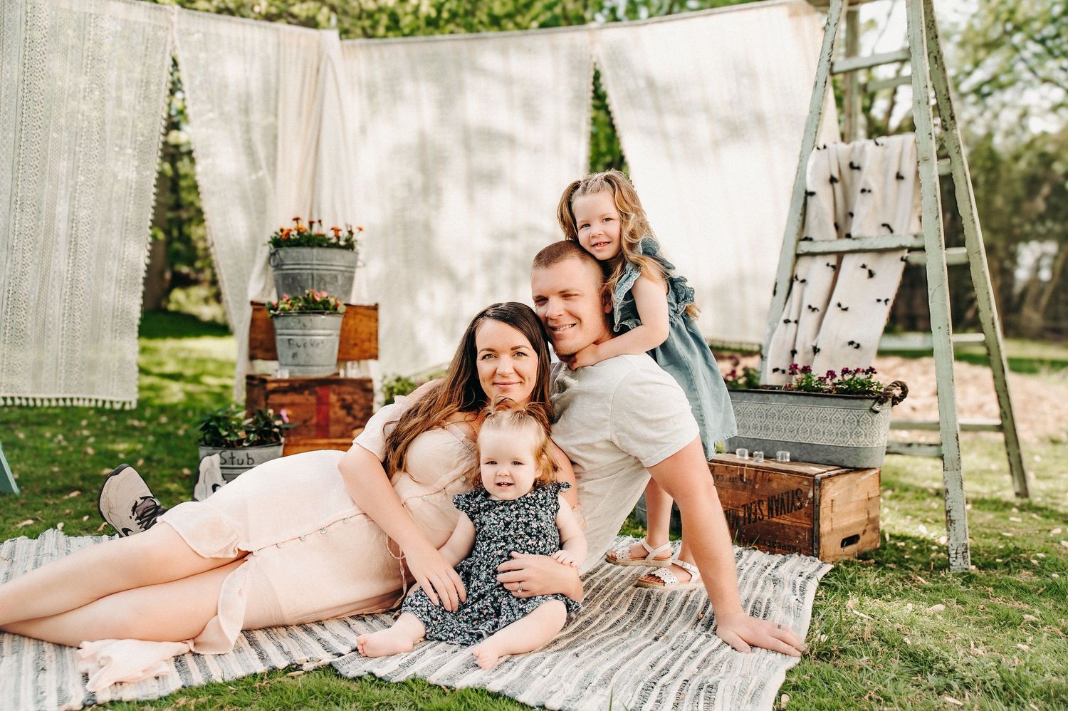 A sweet family moment captured on a white blanket in a sunny outdoor setting.