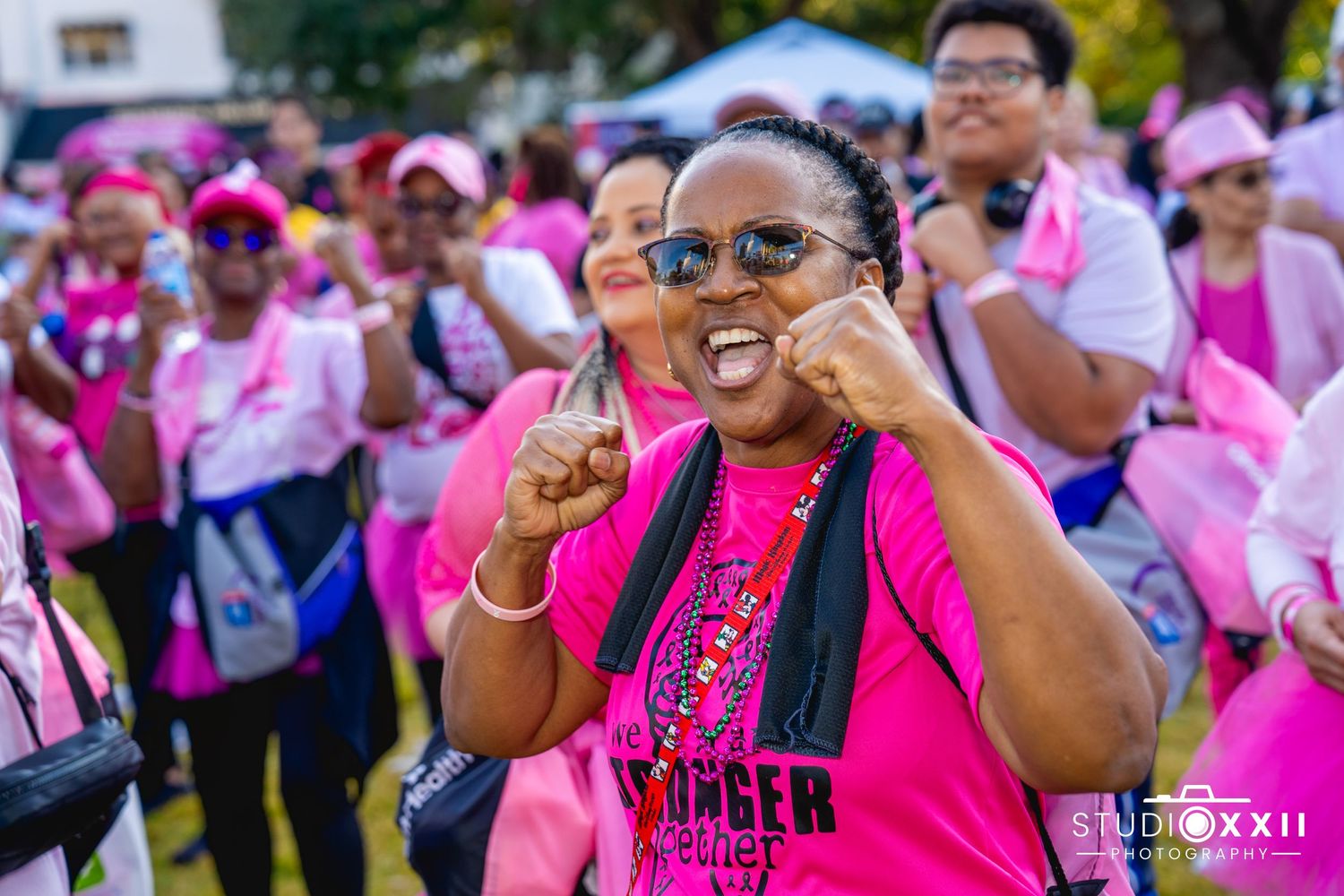 A crowd of participants wearing pink shirts gather at a breast cancer awareness event or charity walk outdoors.