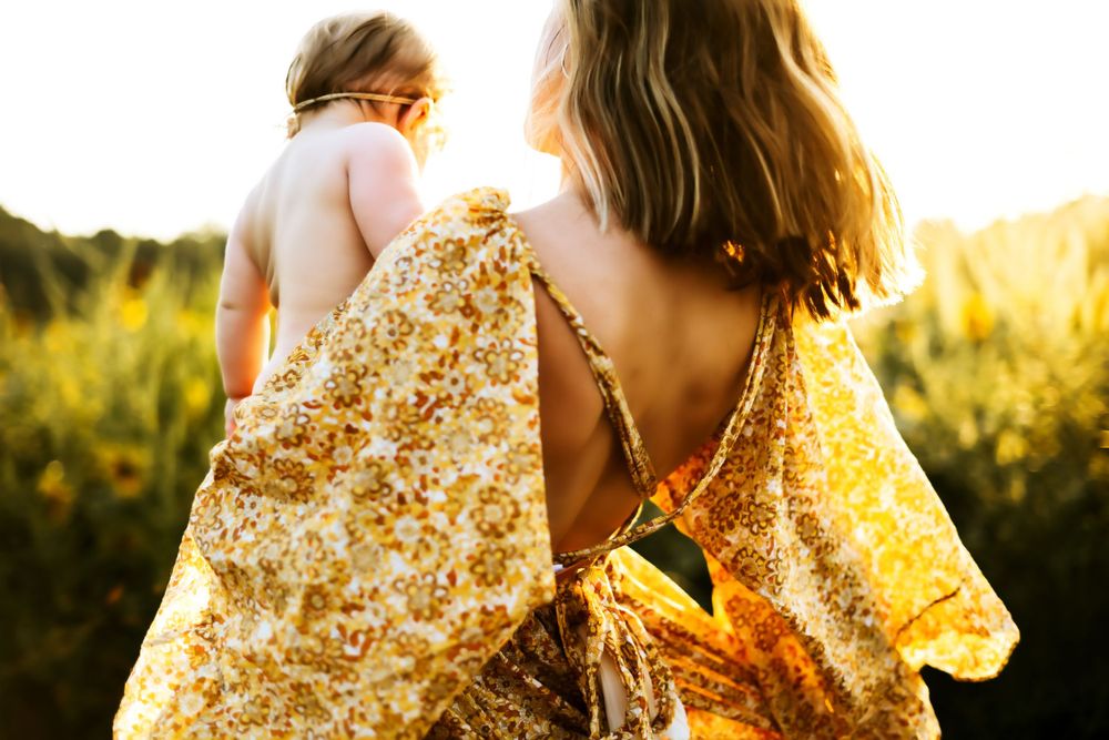 Two figures in flowy floral dresses walking through a sunlit meadow at golden hour.