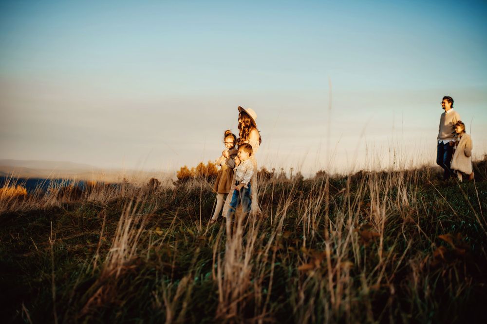 People walking and biking through a tall grass field at golden hour with a soft blue sky backdrop.