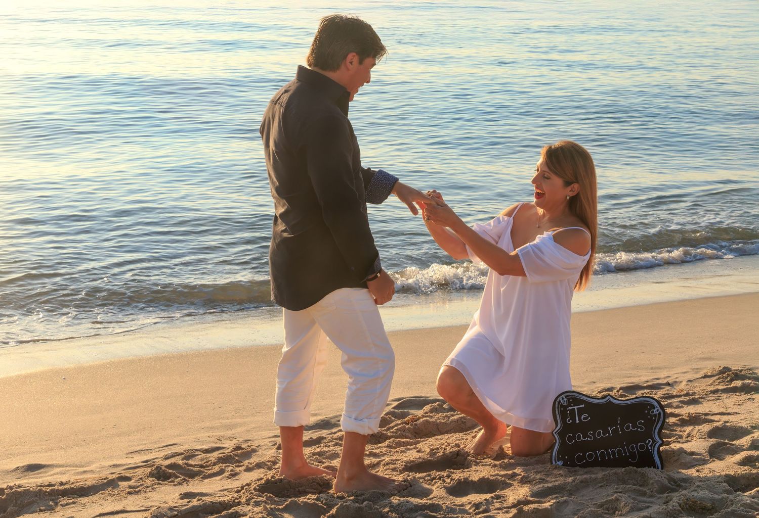 Couple on beach during proposal with special moment sign visible.