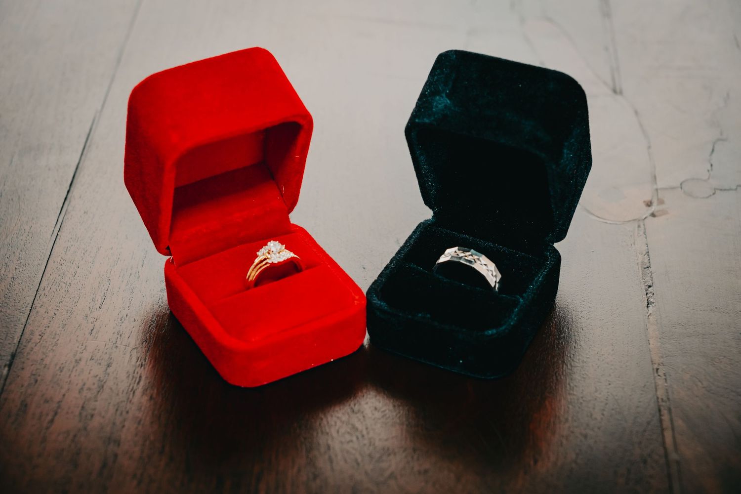 Two elegant engagement rings displayed in red and dark green velvet jewelry boxes.