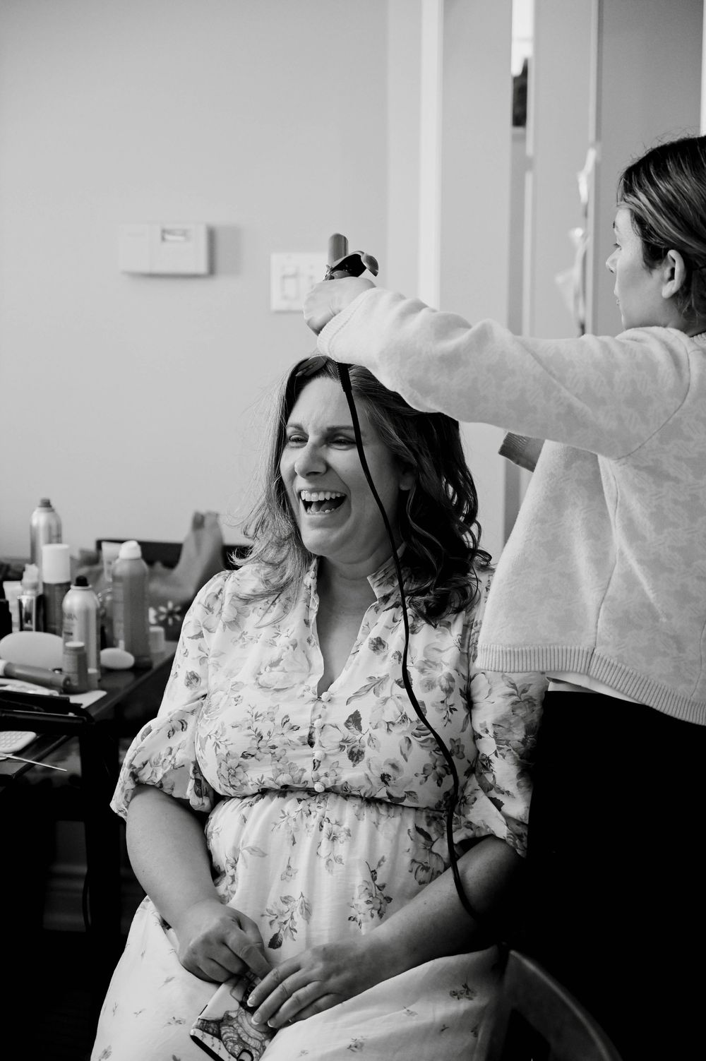 Black and white candid photo of someone laughing joyfully while getting their hair styled in a salon chair.