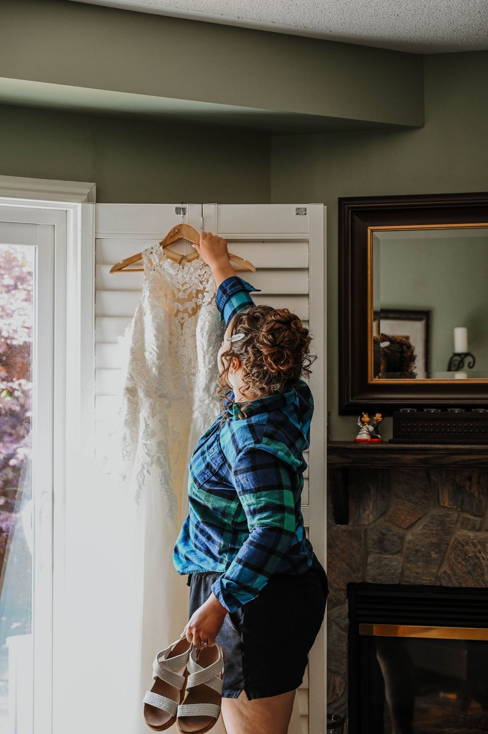 A ginger cat in a blue plaid shirt dances with a wedding dress in a living room.