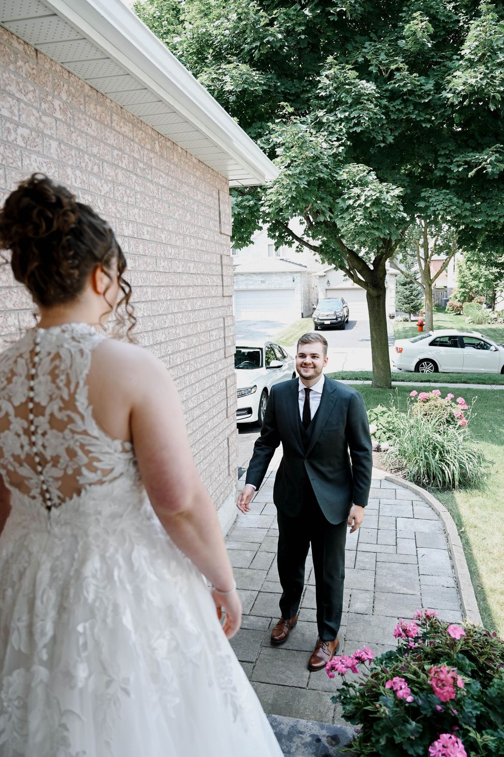 A sweet first look moment captured on a porch with pink flowers blooming during a summer wedding day.