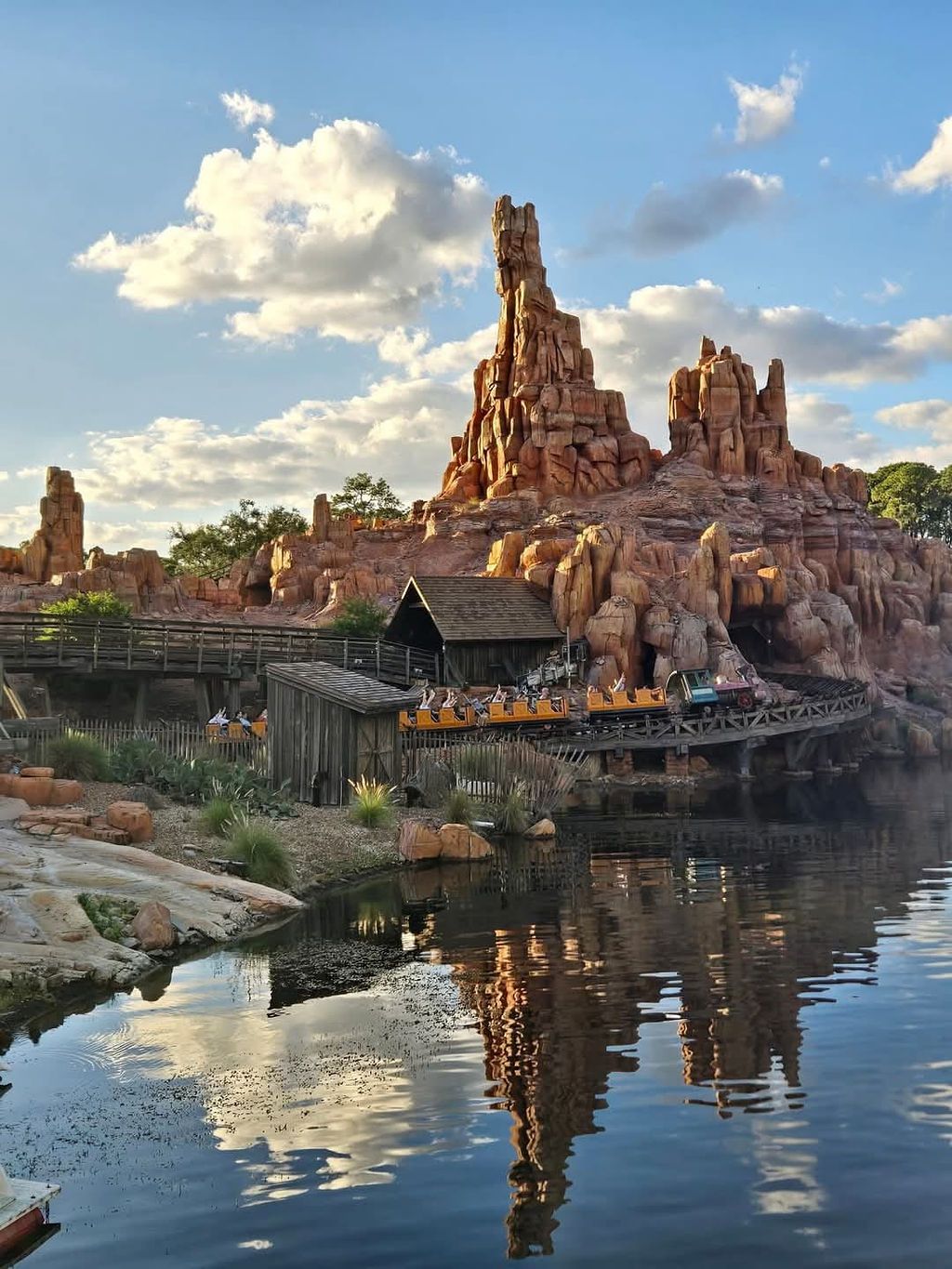 Big Thunder Mountain Railroad at Disney theme park with dramatic rock formations reflecting in calm waters at sunset.