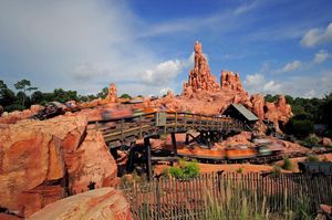 Big Thunder Mountain Railroad roller coaster track winds through red rock formations at Disney World theme park on sunny day.