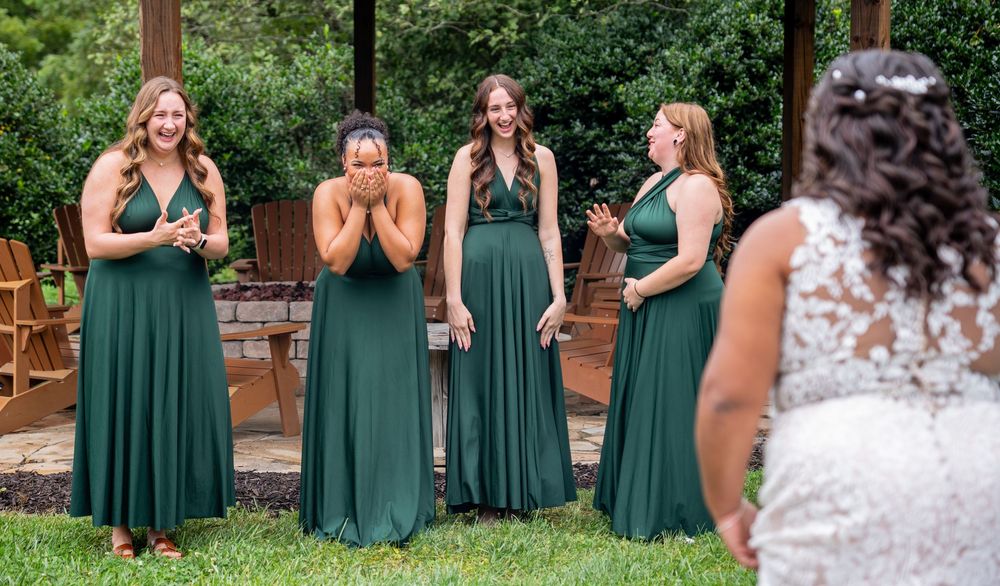 A group in emerald green dresses reacts emotionally during a wedding ceremony outdoors.